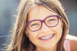 Happy smiling girl with dental braces and glasses. Young cute caucasian blond girl wearing teeth braces and glasses